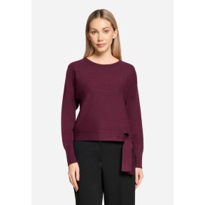 Model i ensfarvet bordeaux strikbluse med rund hals og bindeb�nd forneden. Vist forfra