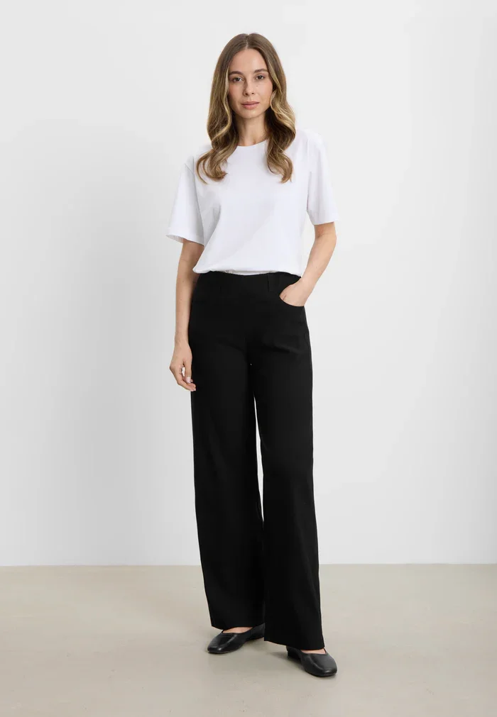 Model ifrt sorte Donna Loose bukser fra Laurie sammen med en lys bluse – moderne look til hverdagsbrug